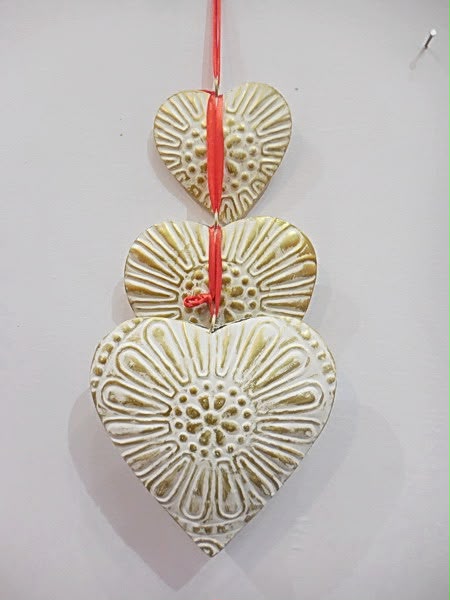 Three embossed heart-shaped metal ornaments on a red ribbon
